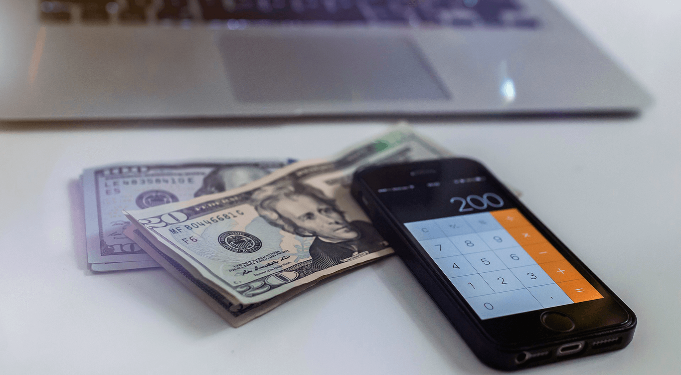 Celular e dinheiro em dólar na frente de um computador