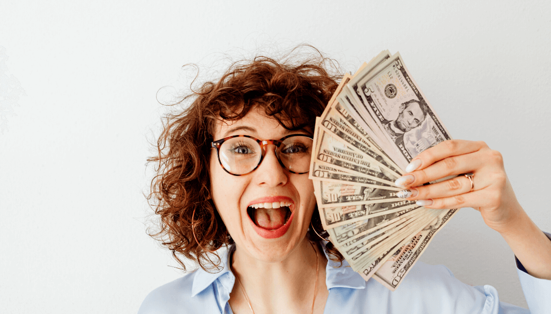 Mulher sorrindo enquanto segura notas de dinheiro.
